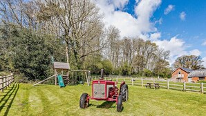 Un campo erboso con un trattore rosso, una struttura giochi in legno e un tavolo da picnic.