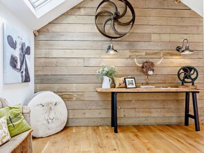 A room with a sloped ceiling, wooden wall paneling, a table with various decorative items, and a mounted light fixture.