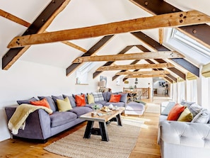Ein geräumiges Loft mit freiliegenden Holzbalken, einem grauen Sofa, einem Couchtisch und Blick ins Innere.