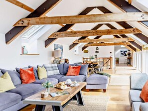 An attic-style living room with exposed wooden beams, a sofa set, a coffee table, and a dining area in the background.