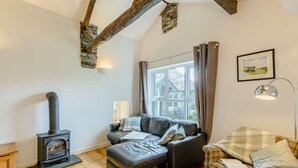 A cozy living room with a fireplace, a sofa, a plaid armchair, and a large window. - 1 Bed in Ambleside (oc-53138) (Ambleside)
