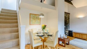 A dining area with a glass table, white chairs, a flower vase, and a painting on the wall. - 1 Bed in Ambleside (oc-53138) (Ambleside)