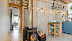 A modern kitchen with a wood-burning stove, a wooden shelf with cookware, and a view to a balcony. - 1 Bed in Llandrindod Wells (oc-53194) (Llandrindod Wells)