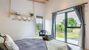 Un dormitorio con una cama, una silla, una ventana con cortinas y una planta en un estante.