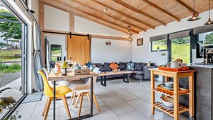 Un interior moderno con comedor, sofá, cocina y ventanas amplias.