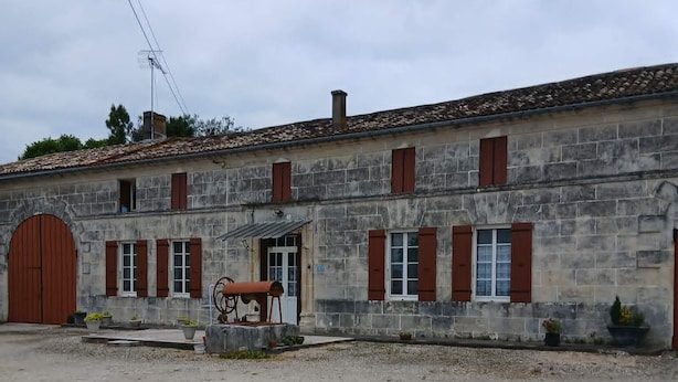 A stone building with a large central door, smaller windows, and a covered area with a horse.