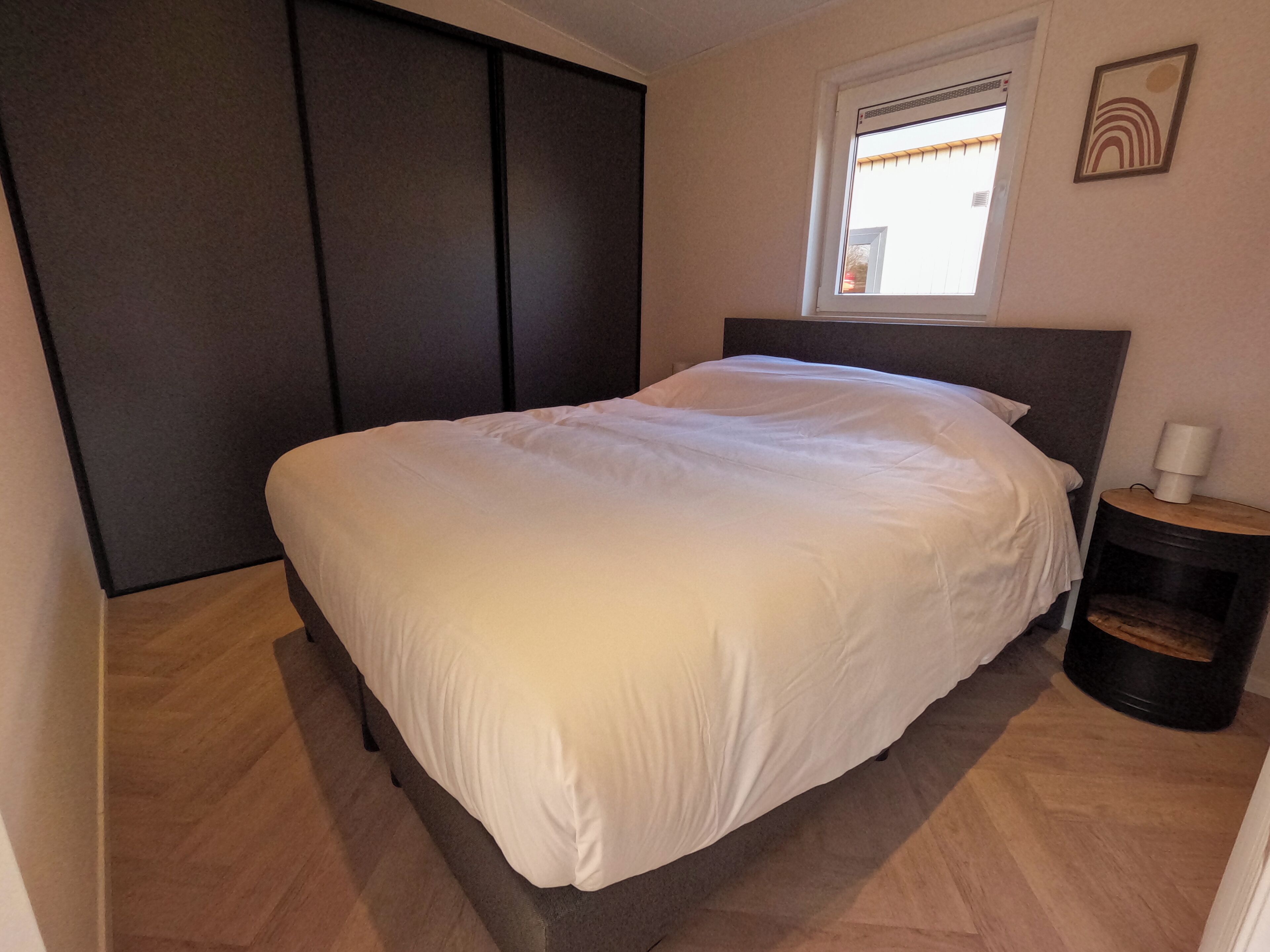 A bedroom with a bed, a nightstand, a window, and a wardrobe.