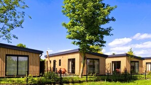 Una hilera de cabañas modernas de madera con ventanas amplias, rodeadas de vegetación y un cielo despejado.