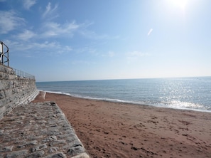 Eine Steinmauer führt zu einem Strand unter blauem Himmel.