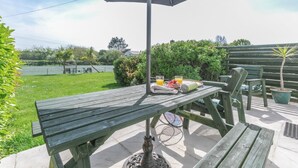 En udendørs terrasse med et træbord, stole og en parasol.
