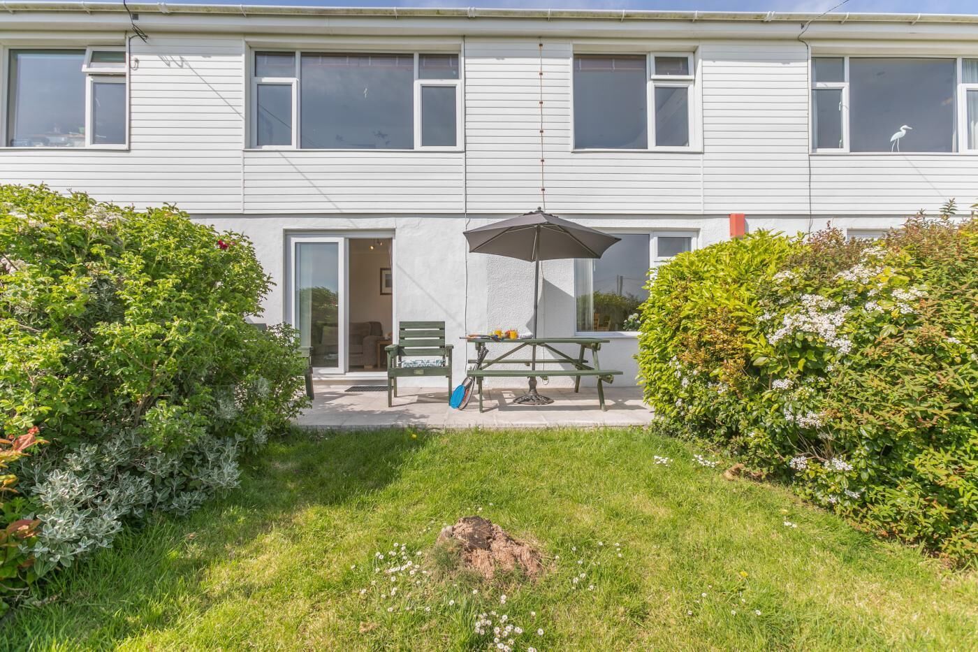 Un bâtiment à deux étages doté d’un patio comprenant une table, des chaises et un parasol.