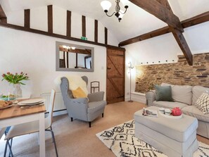 A cozy living room with exposed wooden beams, a stone wall, a dining area with a table set for two, and a sofa with a tray of tea and cups. - 1 Bed in Yelverton (oc-53533) (Yelverton)
