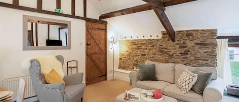 A cozy living room with a stone wall, a wooden ceiling, a sofa, a chair, and a small table with a magazine and teapot.
