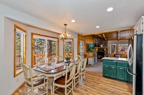 A dining area with a wooden table and chairs, a chandelier, and a stone fireplace. - Big Bear Ski Chalet - Walk to Slopes & Hot Tub (Big Bear Lake)