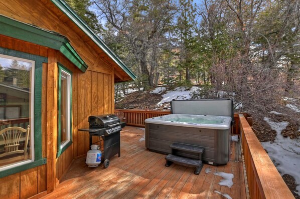 Une terrasse en bois avec un jacuzzi, un barbecue et une chaise.