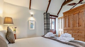 Un dormitorio con cama, lámpara, cuadro, ventana con cortinas y armarios de madera.