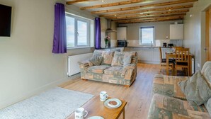Ein gemütliches Wohnzimmer mit Sofa, einem Esstisch mit Teller und Tasse sowie einer Küchenzeile mit Schränken und einem Fenster.