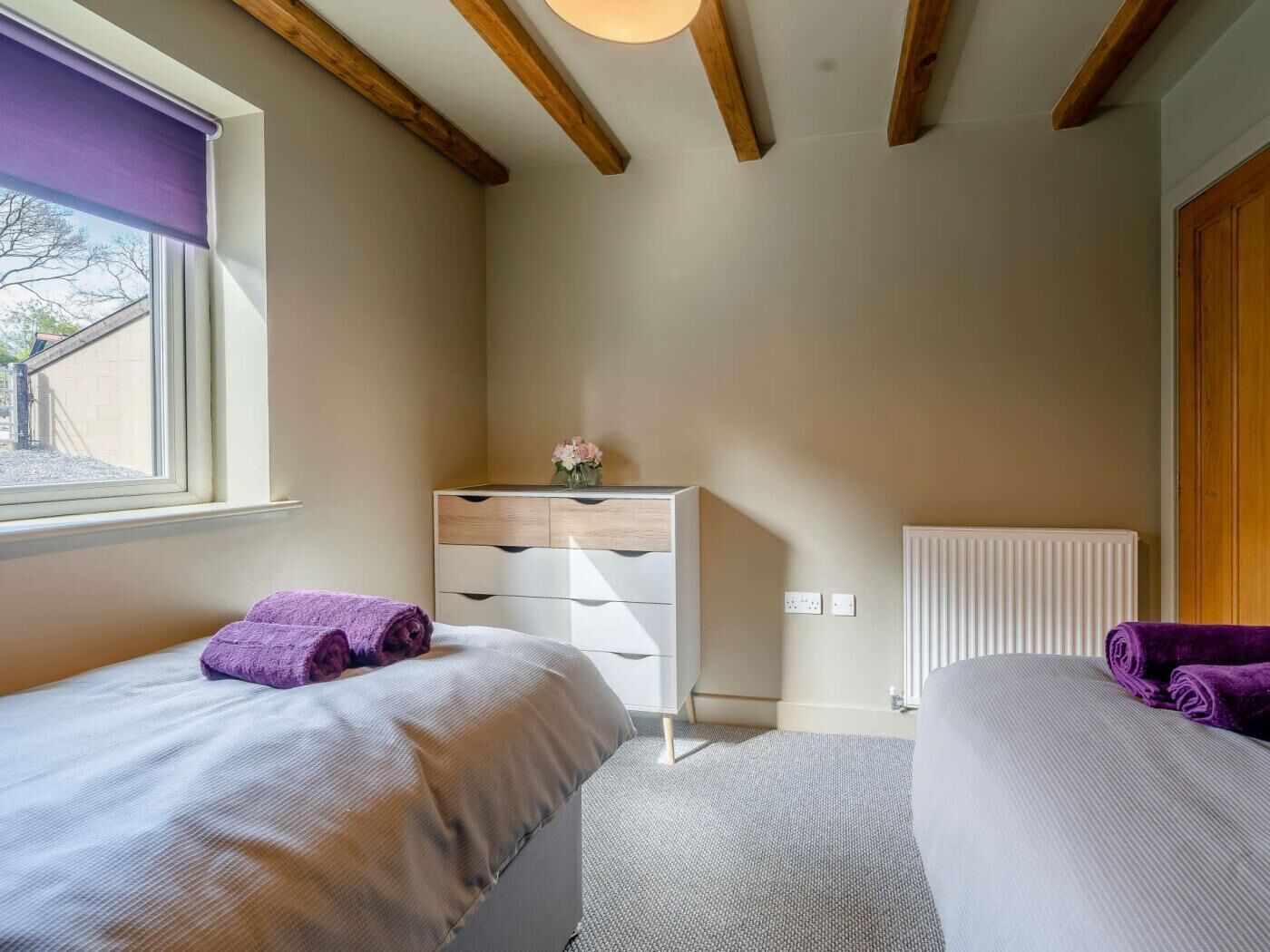 Une chambre avec deux lits, une commode, un radiateur et une fenêtre donnant sur un beau paysage.