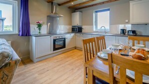 Eine moderne Küche mit Holzbalken, ein Essbereich mit Tisch für zwei Personen und ein Ausblick ins Freie durch ein Fenster.