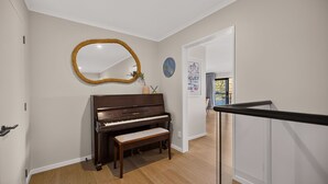 A piano in a hallway with a mirror and artwork on the wall. - Sunrise Retreat - lake and mountain views (Queenstown)