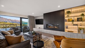 A modern living room with a fireplace, a television, and a bookshelf. - Sunrise Retreat - lake and mountain views (Queenstown)
