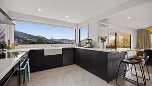 A modern kitchen with a large island, dark cabinetry, and a view of mountains. - Sunrise Retreat - lake and mountain views (Queenstown)