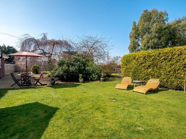 Un jardin avec une table de patio, des chaises, un fauteuil de jardin en bois et une haie.