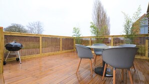 Eine Holzterrasse mit Tisch, Stühlen, einem Grill und einem Bambuszaun.