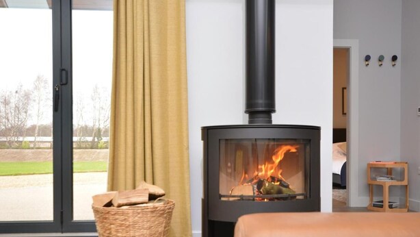 Ein modernes Wohnzimmer mit Kaminofen mit Glasfront, einem Korbwicker-Holzvorrat und einem Ledersofa.