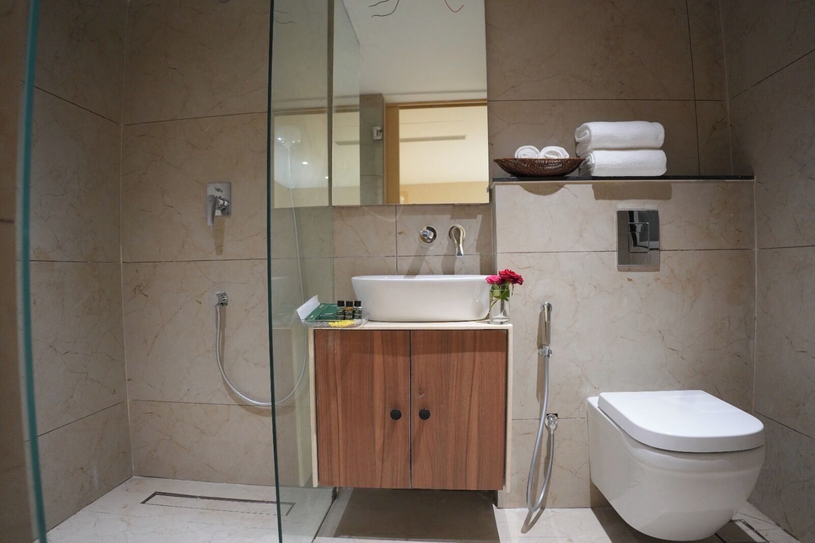 A modern bathroom with a glass-enclosed shower, a wooden cabinet, a white sink, and a toilet.