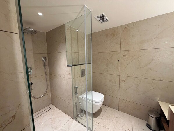 A modern bathroom with a glass-enclosed shower, a toilet, and a trash bin.