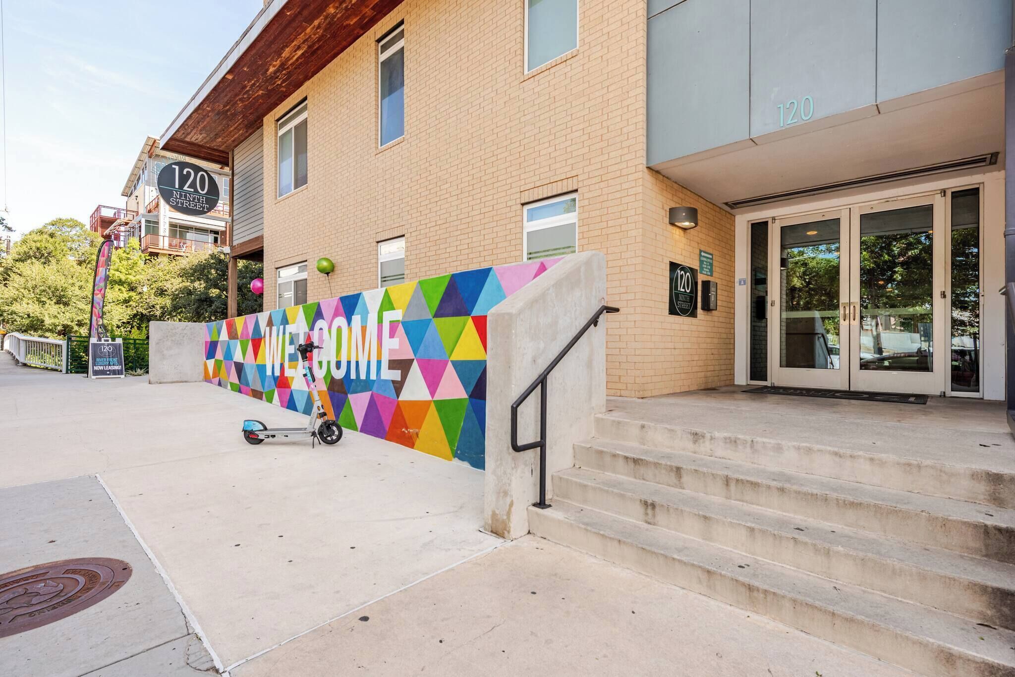 A building with a colorful geometric wall, a scooter, and a staircase leading to the entrance.