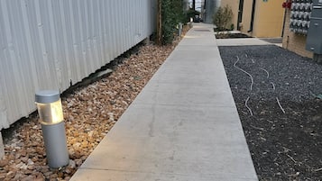 A concrete pathway flanked by a metal wall and a landscaped area with rocks and grass.
