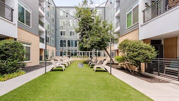 A courtyard with lounge chairs, a small tree, and a building with balconies.