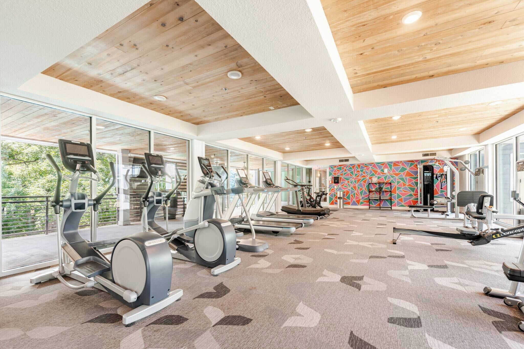 Une salle de sport équipée de divers appareils d’exercice, dotée de grandes fenêtres et d’un mur aux couleurs vives.