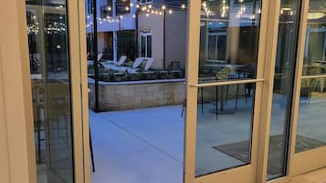 A glass door entrance to a building with outdoor seating and string lights.