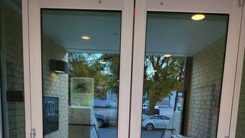 A double door entrance with glass panels and a metal handle, leading to a brick wall.