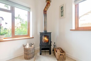 A room with a wood-burning stove, two wicker baskets, and a window with a view of greenery.