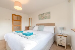 A hotel room with a bed, a bedside table with a lamp, a mirror, and a painting on the wall.