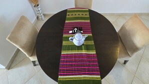 Une table de salle à manger ronde, agrémentée d’un chemin de table décoratif, d’une théière et de deux chaises.