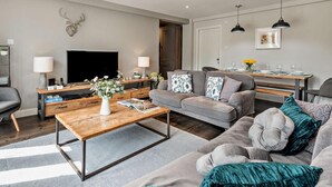 Ein modernes Wohnzimmer mit Sofa, Couchtisch, Fernseher und einem Essbereich mit Tisch und Stühlen.