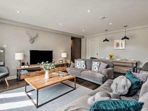 Ein modernes Wohnzimmer mit Sofa, Couchtisch, Fernseher und einem Essbereich mit Tisch und Stühlen.