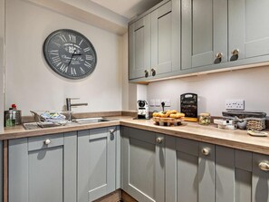 A kitchen with grey cabinets, a round wall clock, a sink, and a coffee maker. - 3 Bed in Bakewell (oc-53896) (Bakewell)