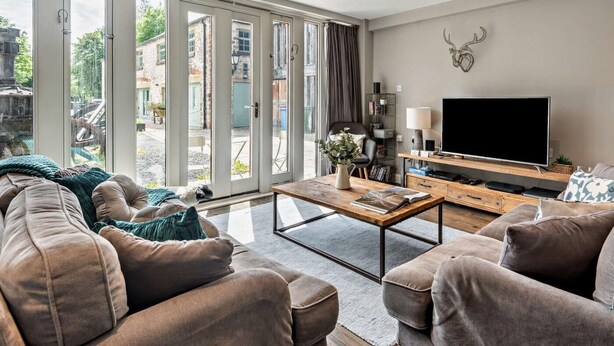 Ein modernes Wohnzimmer mit einer Couch, einem Couchtisch, einem Fernseher und großen Fenstern.