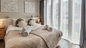 Ein modernes Hotelzimmer mit einem großen Bett, zwei Nachttischen und einem Blick auf die Stadt durch große Fenster.