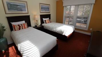 A hotel room with two beds, a window with blinds, a lamp, and framed pictures on the wall.