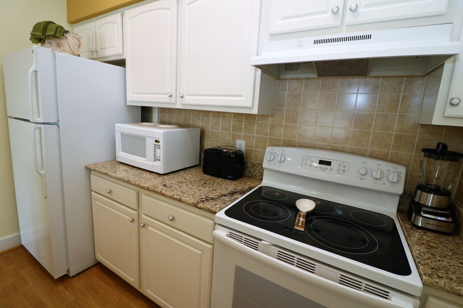 A kitchen with white cabinets, a microwave, a toaster, a stove, and a blender.