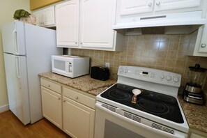 Une cuisine avec des meubles blancs, un four à micro-ondes, un grille-pain, une cuisinière et un mixeur.