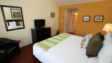 A hotel room with a bed, a TV on a dresser, a desk, and a chair.