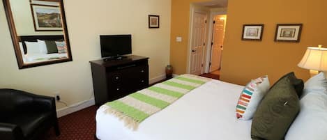 Una habitación de hotel con una cama, un televisor en una cómoda, un escritorio y una silla.
